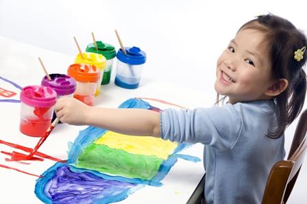 Little girl smiling at the camera while finger painting